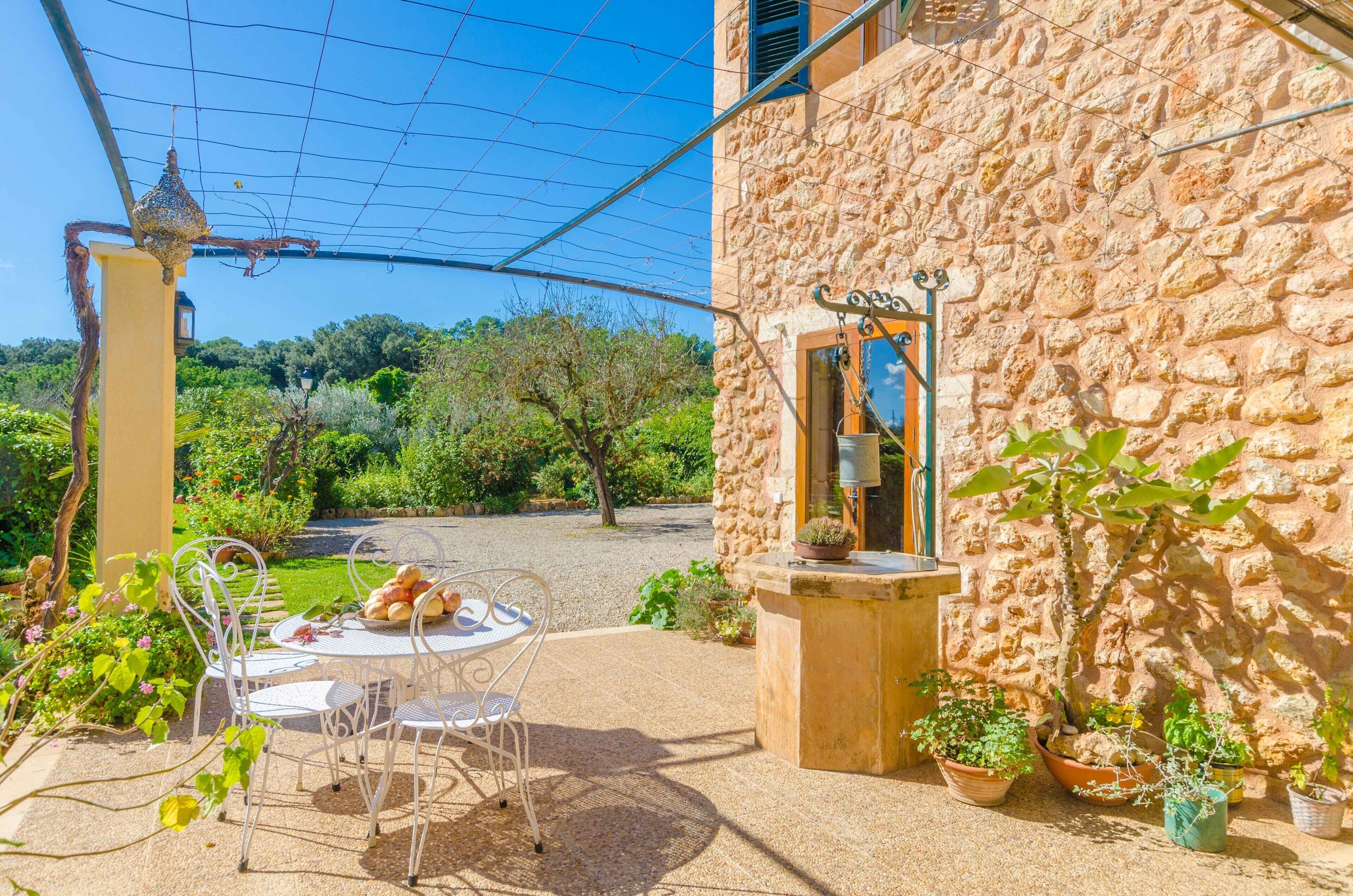 Edificio de piedra con un patio jardín, mobiliario exterior y plantas en macetas.
