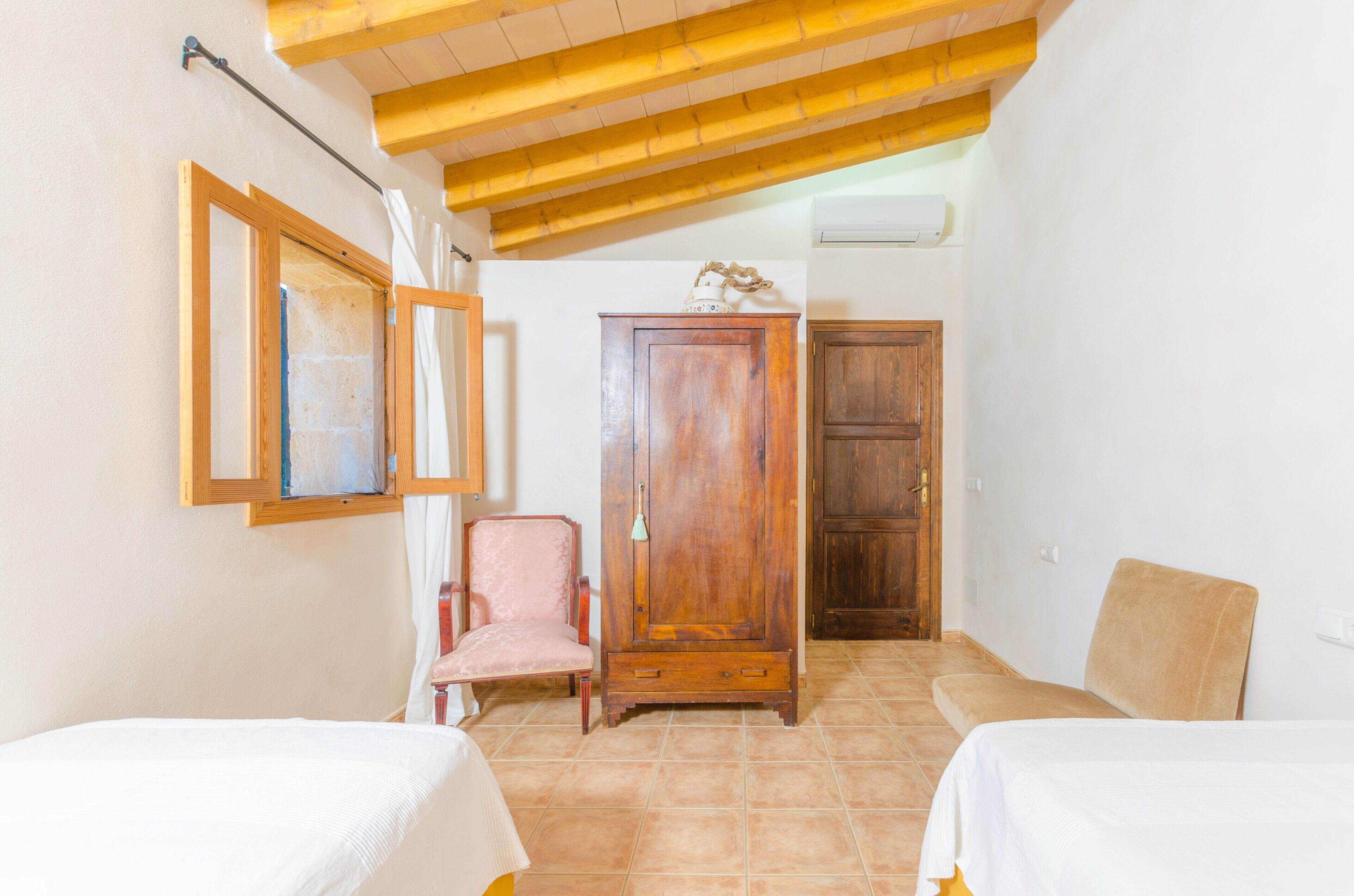 A room with two beds, a wooden wardrobe, a chair, and a cabinet.