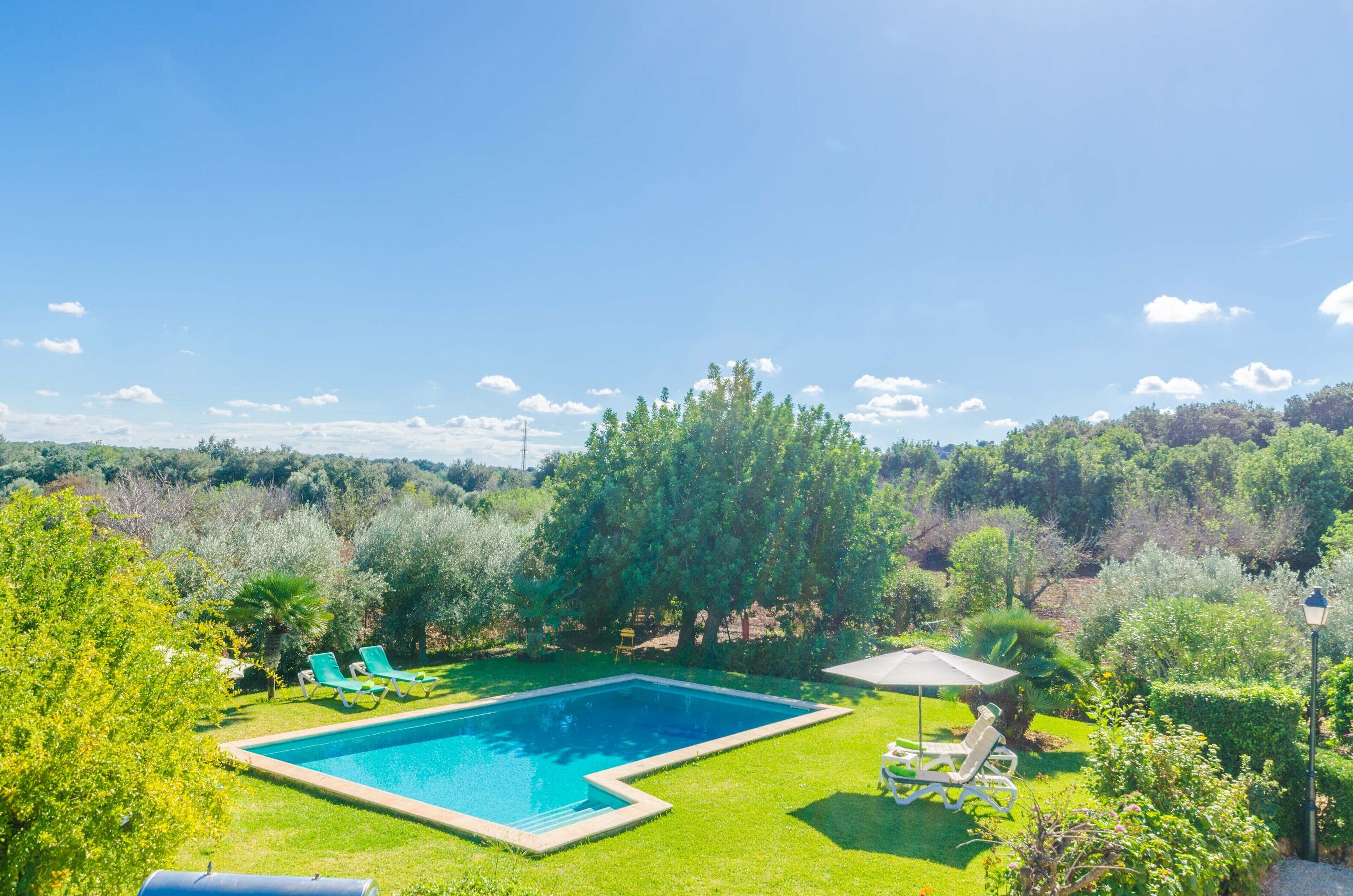 Une piscine rectangulaire entourée d’une pelouse bien entretenue, avec deux chaises longues et une petite table placée sous un auvent.