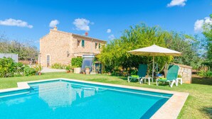 A swimming pool with lounge chairs and an umbrella, surrounded by a garden and a stone building. - SA MATA - Spectacular Majorcan finca with private pool enclosed by the trees and greenery (Campanet)