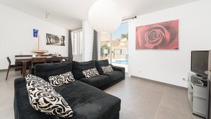 Un salon moderne avec un canapé d’angle, un coin repas et une grande fenêtre.
