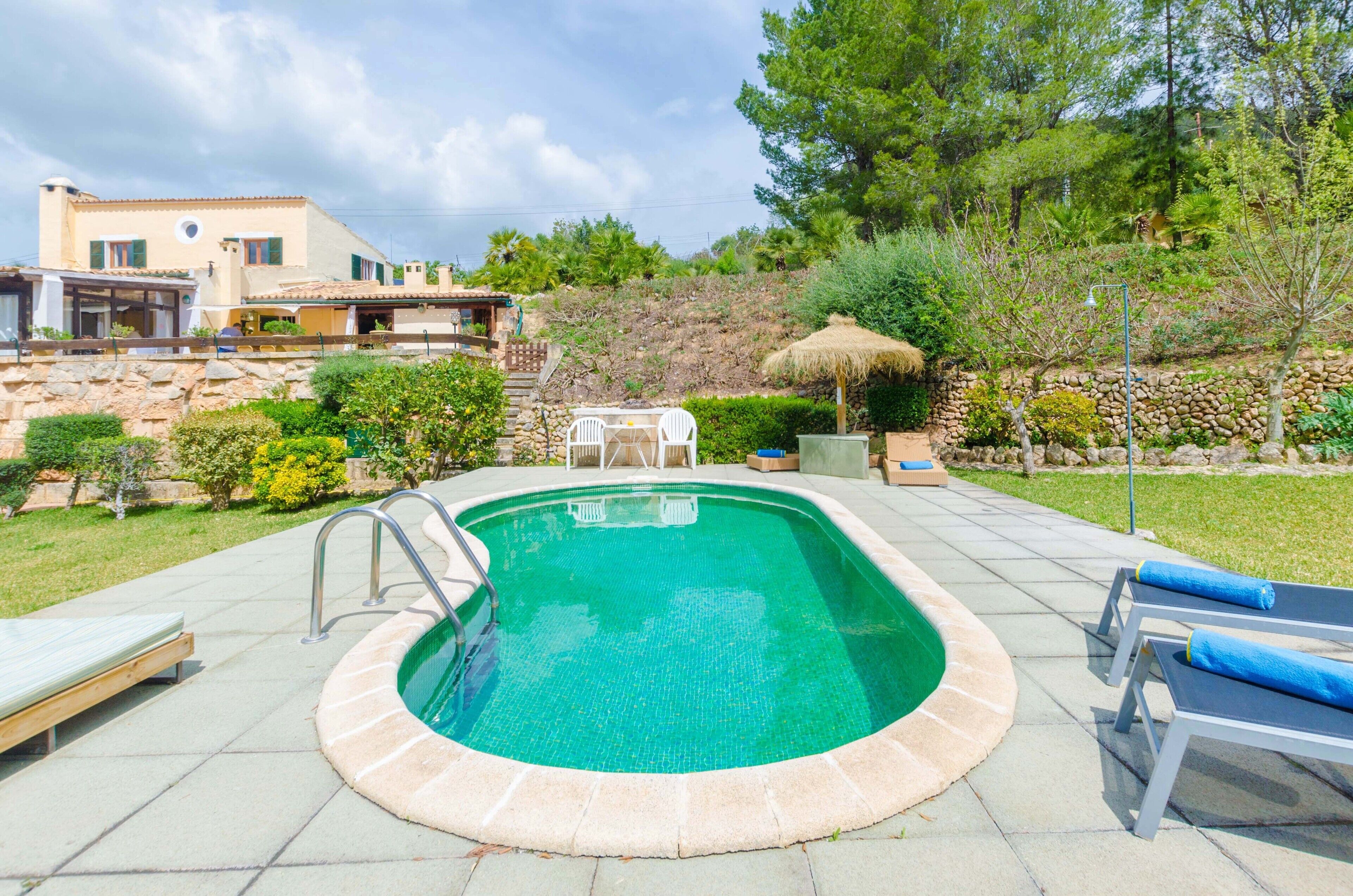 A swimming pool with a stone border, a lounge chair, and a small table.