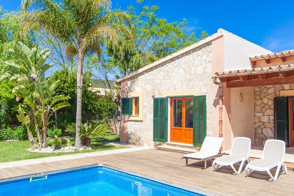 A poolside area with a stone building, green shutters, and lounge chairs.