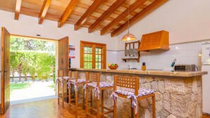 Une cuisine dotée de plans de travail en pierre, de tabourets de bar en bois, d’un luminaire suspendu et offrant une vue sur l’extérieur.