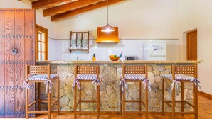 Une cuisine avec un îlot central en pierre, des chaises en bois, un luminaire suspendu et une porte en bois.