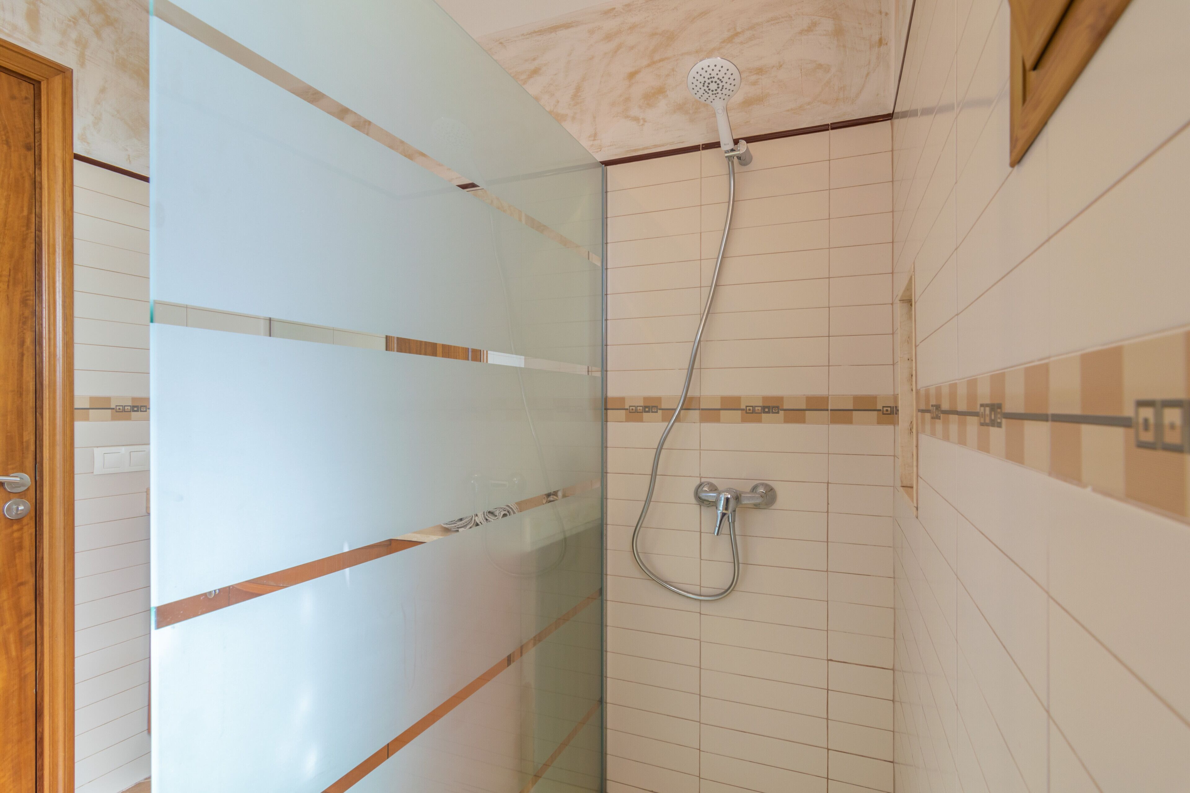 A bathroom with a glass shower enclosure, tiled walls, and a wooden door.