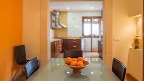 Uma área de refeições com mesa de vidro, cadeiras e uma tigela de laranjas.