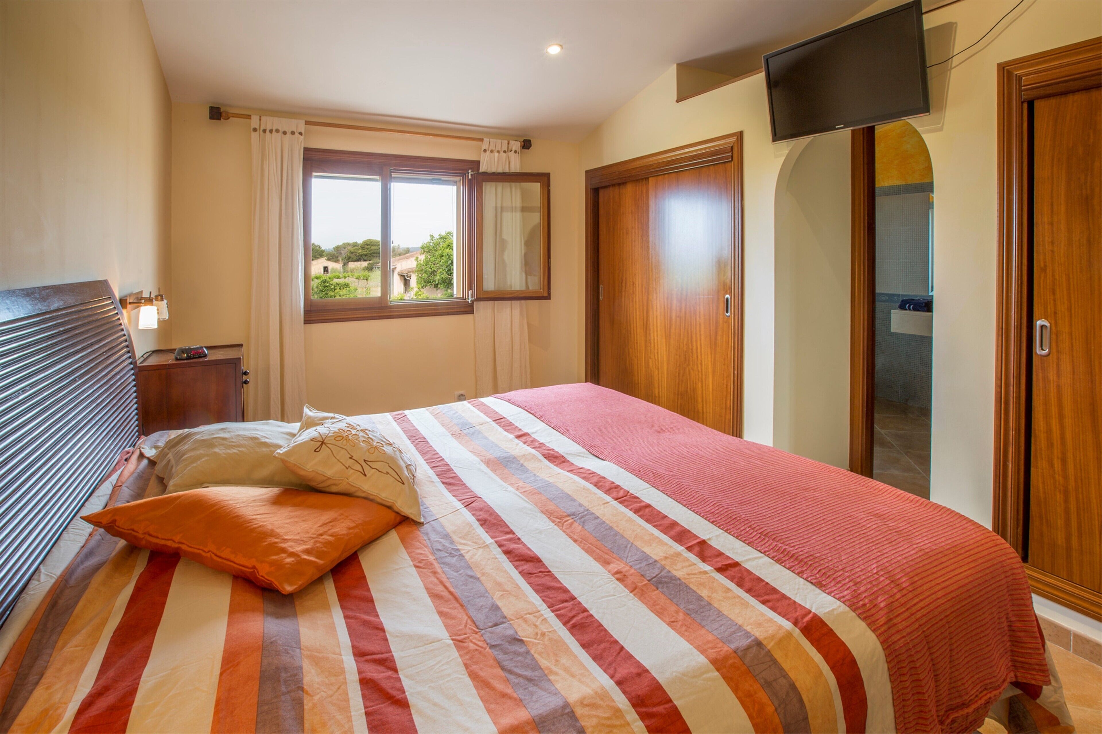 A bedroom with a bed, a television mounted on the wall, and a window with curtains.