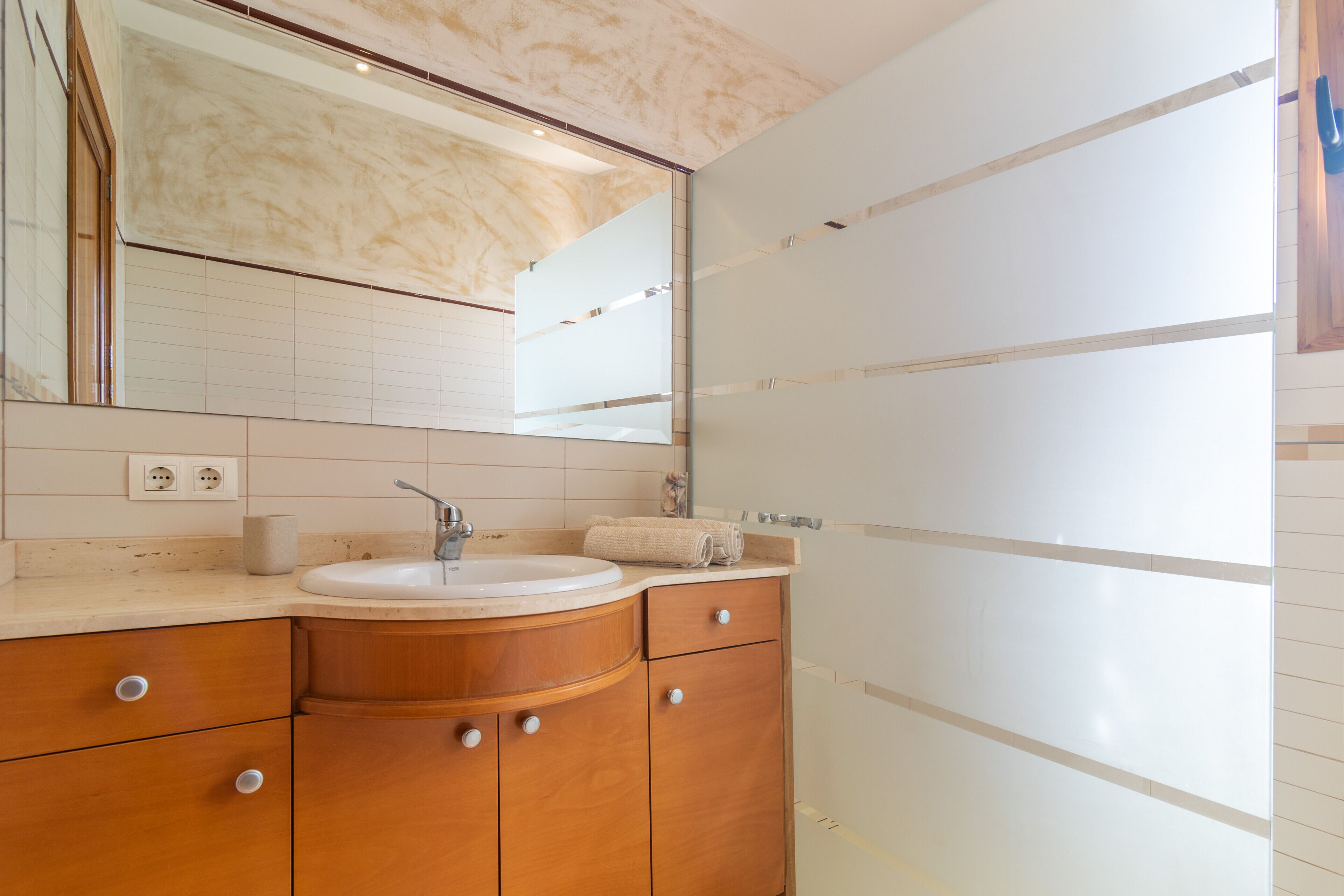 A bathroom with a wooden vanity, white tiles, a mirror, and a sink.