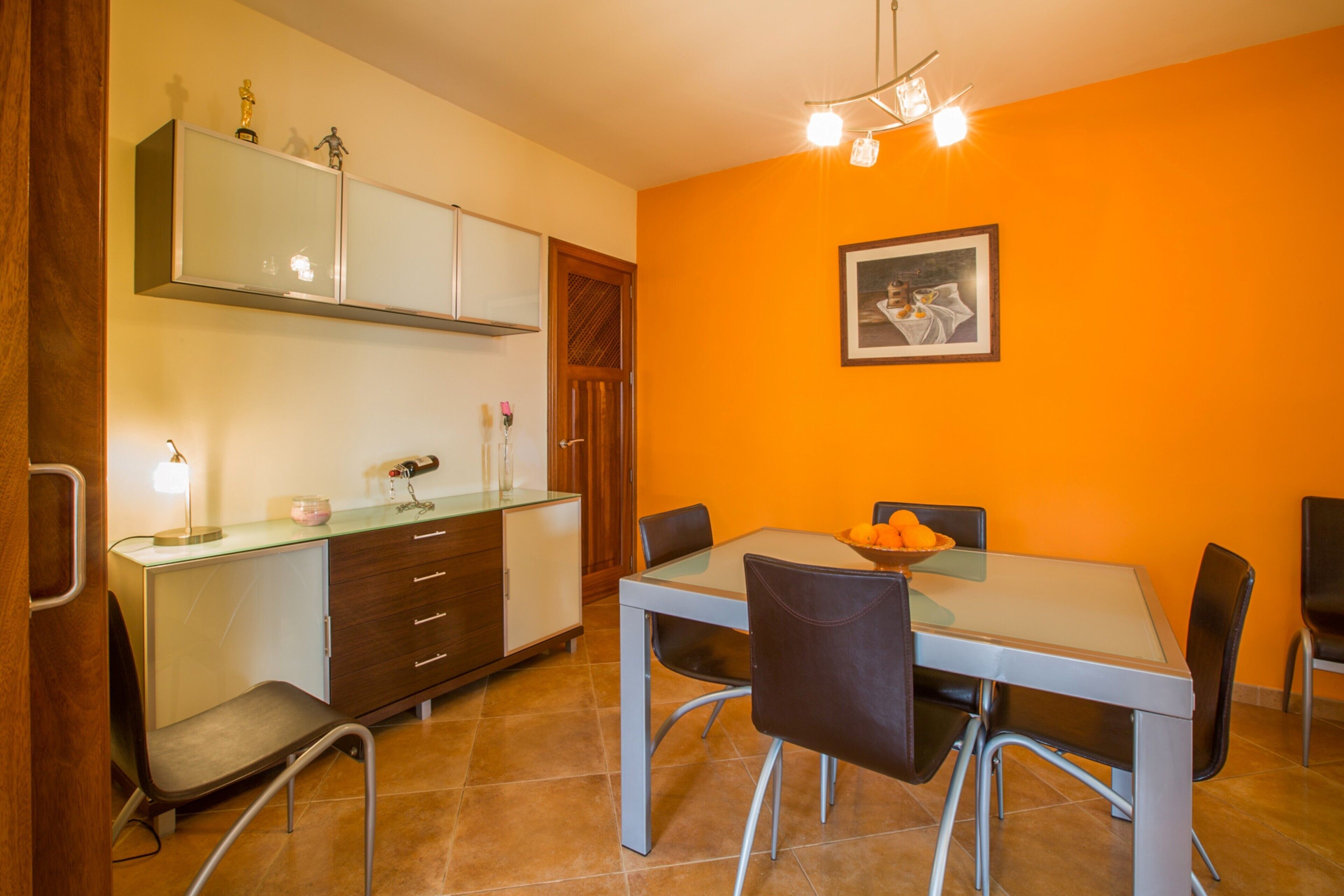 A dining area with a glass table, chairs, a cabinet, and a painting on the wall.