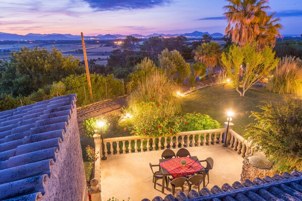 A patio with a table and chairs, surrounded by greenery and a view of distant mountains.