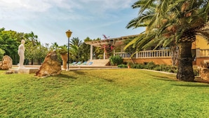 Un jardín cuidado con una estatua, palmeras y una zona de piscina.