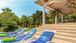 Un área junto a la piscina con sillones reclinables azules y una zona de estar techada.