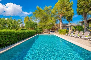 A clear swimming pool with lounge chairs and a stone building in the background.