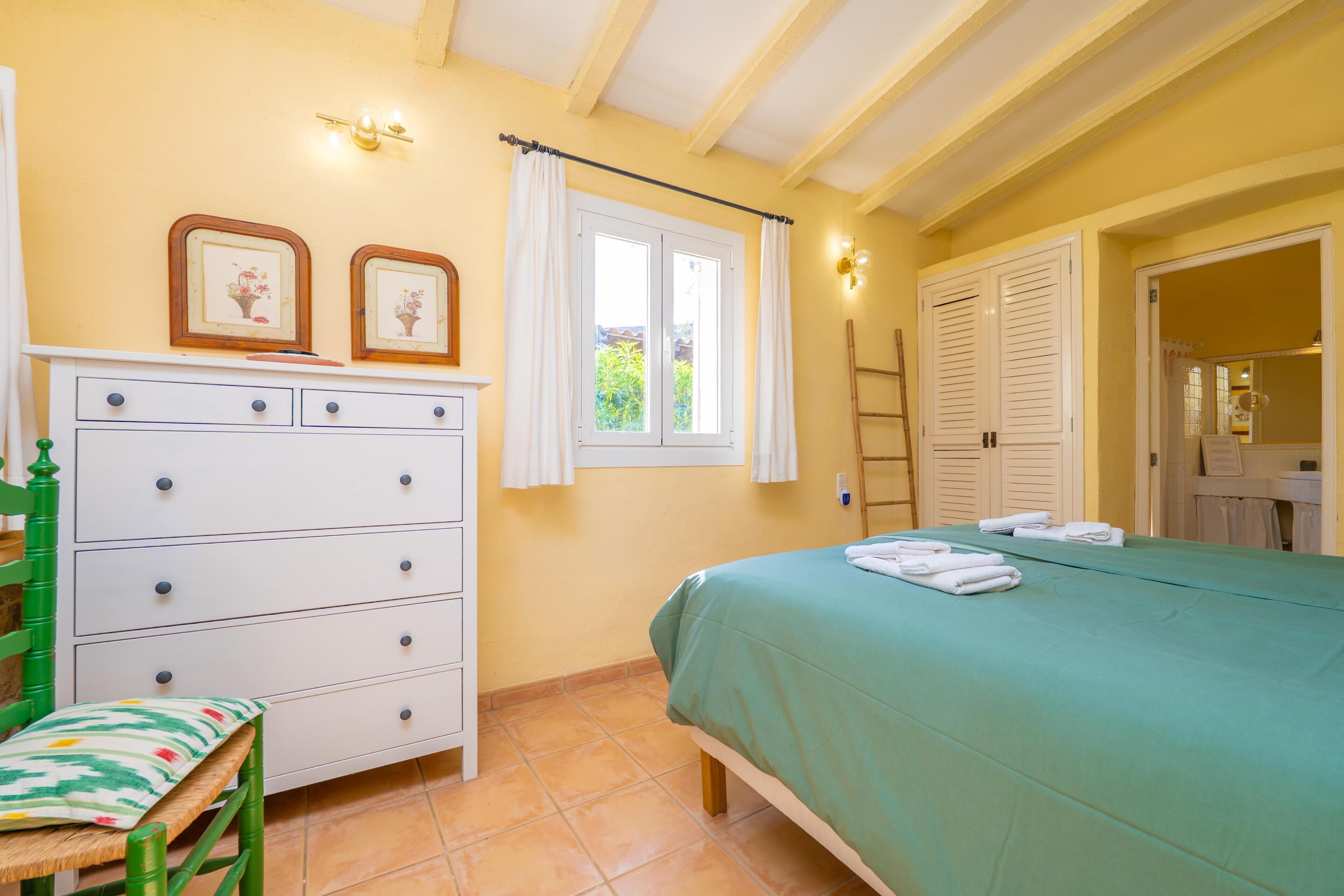 Un dormitorio con cama, cómoda, silla, ventana y puerta.