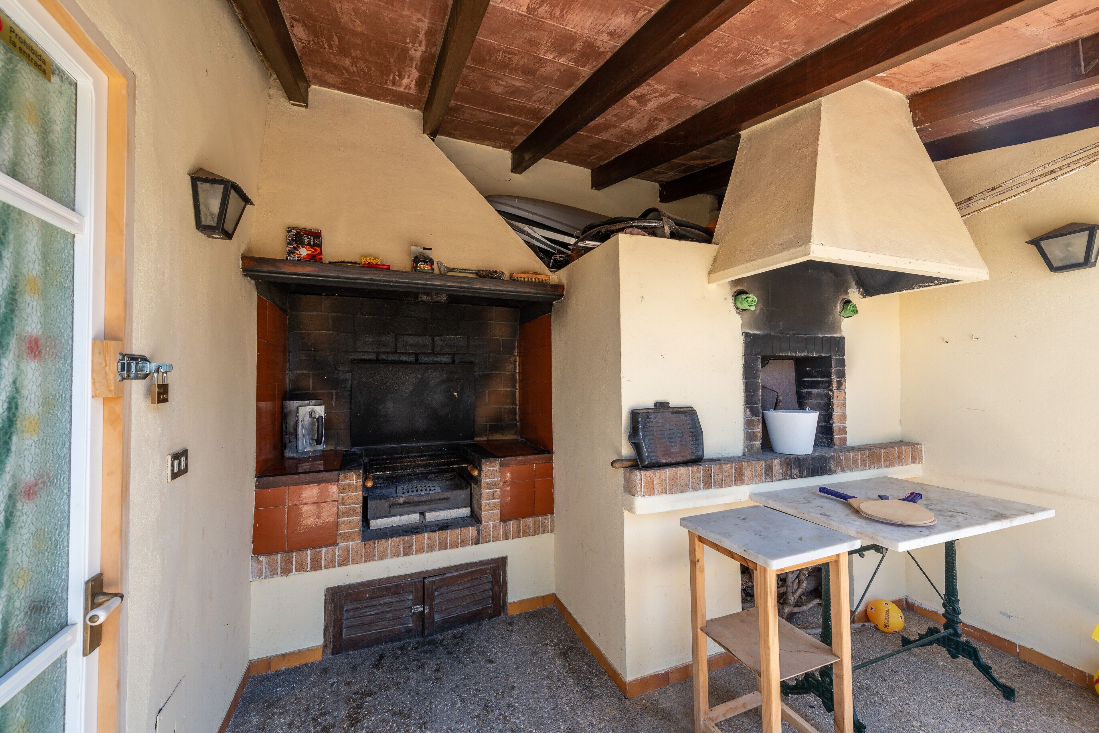 Une cuisine avec un four en briques, une table avec une planche à découper et un luminaire suspendu.