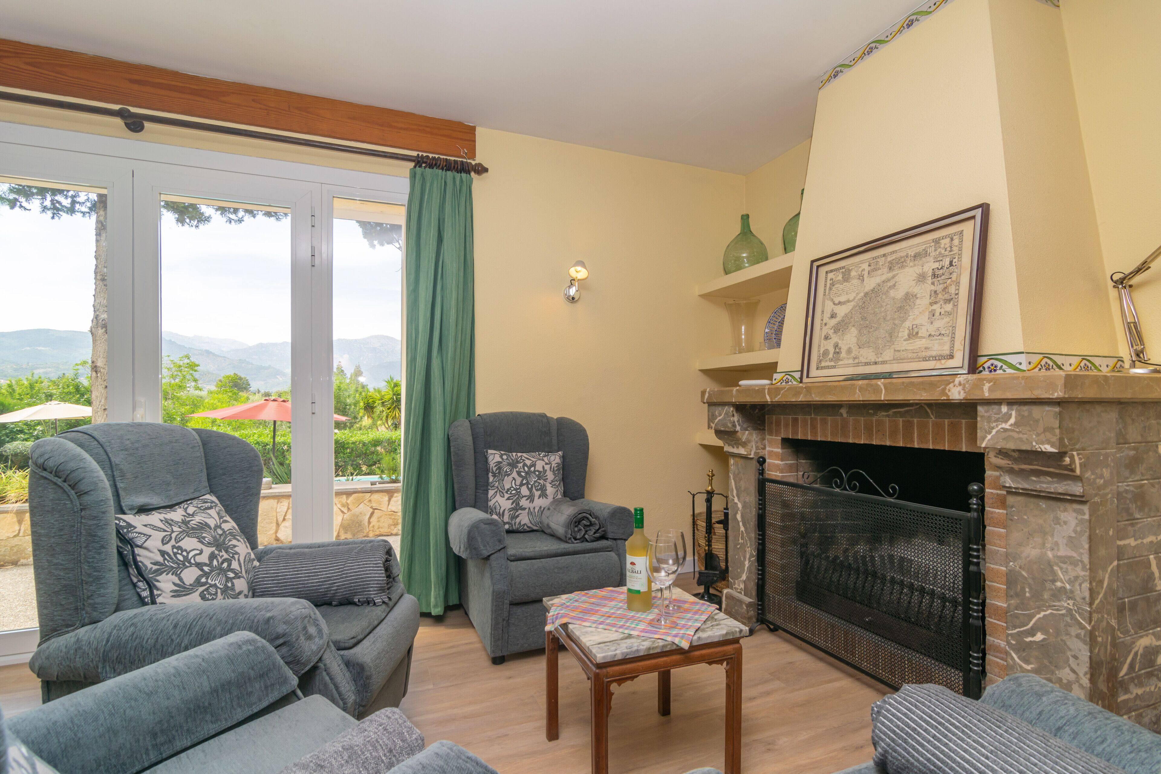 A living room with a fireplace, two sofas, a table with a bottle and glass, and a view through large glass doors.