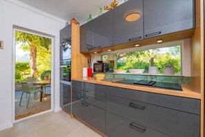 A modern kitchen with dark cabinets, a wooden countertop, and a window overlooking a garden.