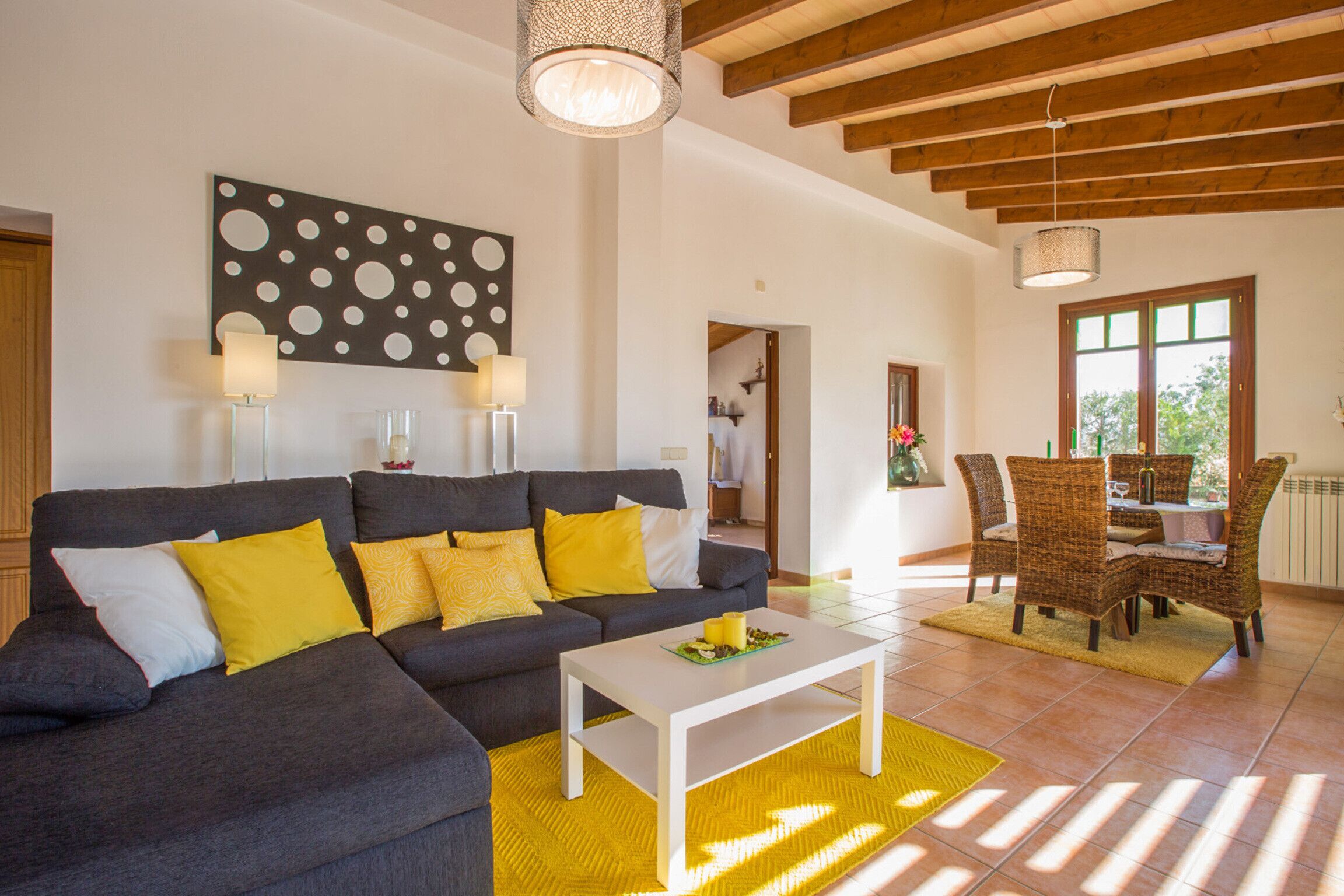 Ein modernes Wohnzimmer mit grauem Sofa, gelben Kissen, einem weißen Couchtisch und einem Essbereich mit Korbstühlen.