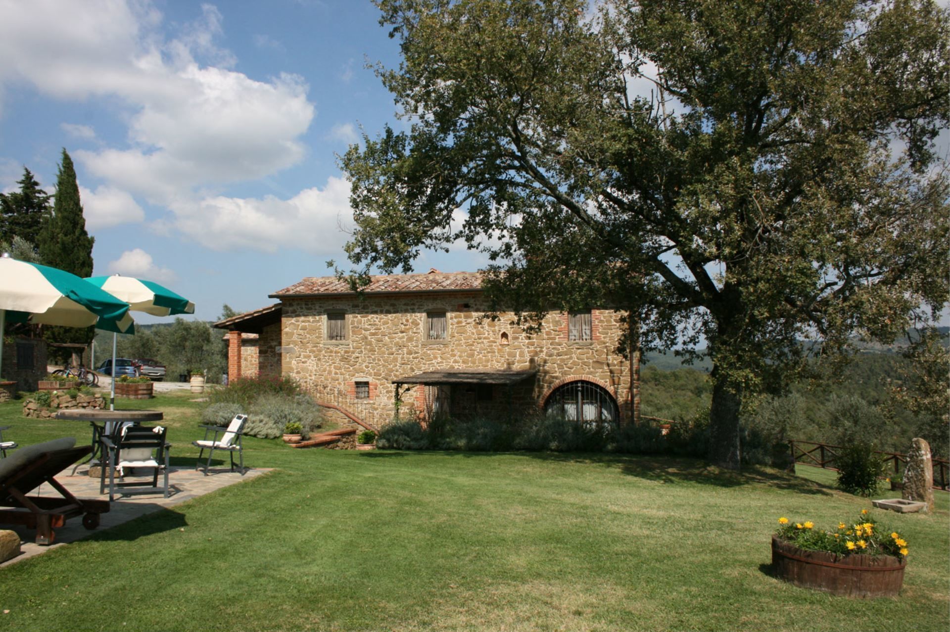 A stone building with a tiled roof, surrounded by a well-maintained lawn and a large tree.