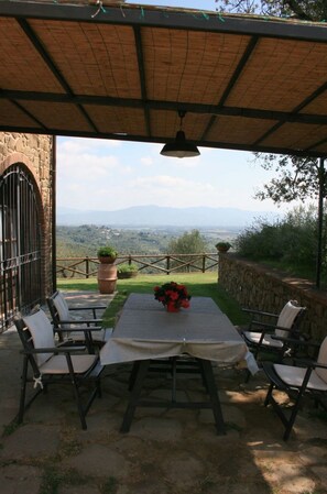 Une terrasse extérieure avec une table et des chaises, une vue sur la campagne et un mur en pierre.