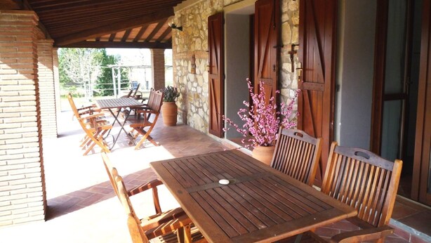 Une terrasse couverte avec une table et des chaises en bois, des murs en pierre et des volets en bois.