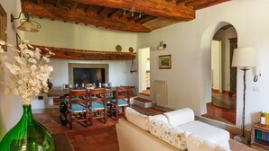 A cozy living room with a fireplace, wooden beams, a dining area, and a sofa. - Apartment with pool, A/C, WIFI, TV, terrace, pets allowed, panoramic view, close to Greve In Chianti (Mercatale)