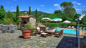 An outdoor patio area with stone flooring, a stone-built fireplace, outdoor seating, and a swimming pool. - Stunning private villa with private pool, hot tub, A/C, WIFI, TV, panoramic view, close to Florence (San Casciano In Val Di Pesa)