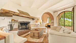A cozy living room with a fireplace, white sofas, a wicker ottoman, and a view of greenery through large windows. - Private Villa with WIFI, hot tub, private pool, TV, patio, panoramic view, close to Greve In Chianti (Lucarelli)
