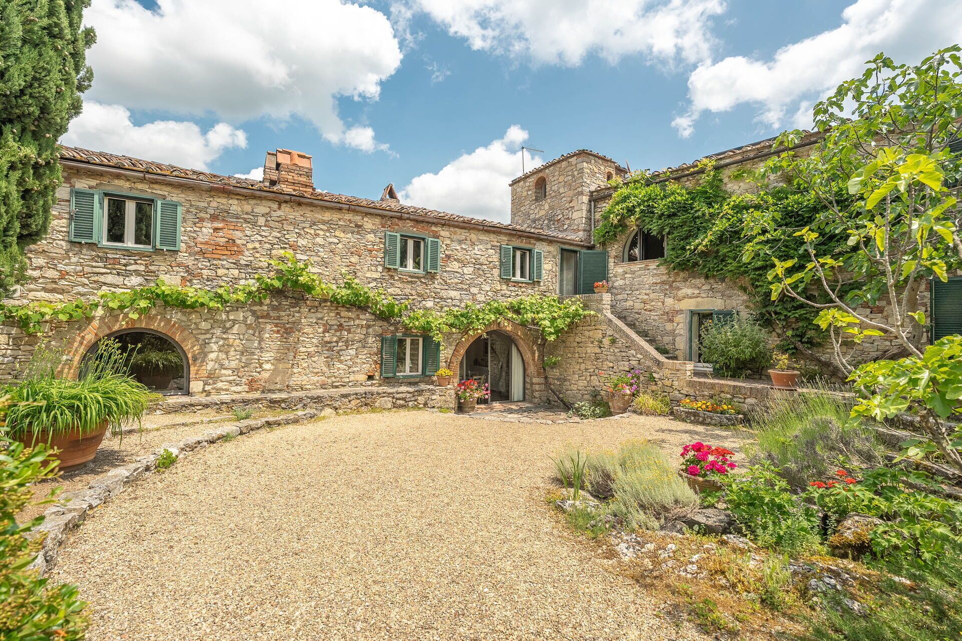 A stone building with a gravel courtyard, arched doorways, and green shutters.