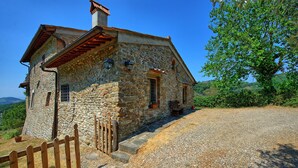 A stone house with a sloped roof, a wooden fence, and a gravel driveway.