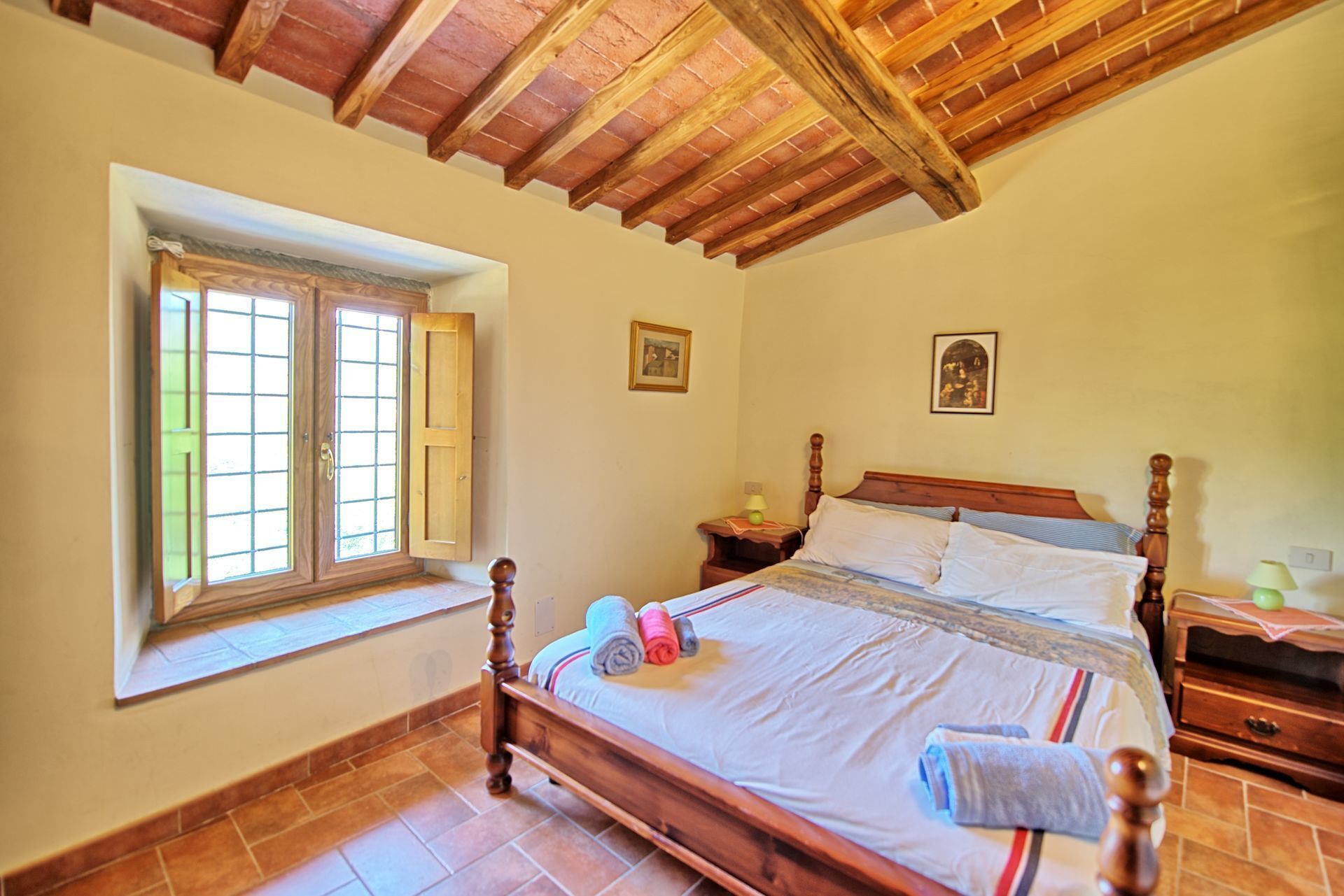 Une chambre à coucher avec un lit en bois, une fenêtre avec des volets, une table de chevet et une commode.