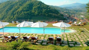 Piscina con tumbonas y sombrillas, rodeada por un jardín ajardinado y vistas a un paisaje montañoso.