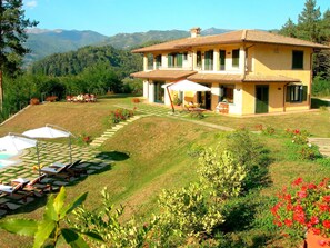 Una casa de dos pisos con un patio, mobiliario exterior y vistas a montañas.