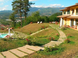 Un jardín en pendiente con piscina, mobiliario exterior y vistas a montañas.