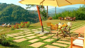 Une terrasse avec une table et des chaises, entourée d’un jardin offrant une vue sur les montagnes.