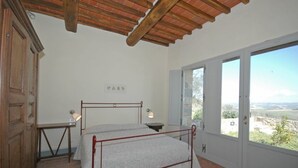 A bedroom with a bed, a nightstand, a lamp, and a view of the outdoors. - Nice apartment for 3 guests with A/C, pool, TV, pets allowed and panoramic view (Montalcino)