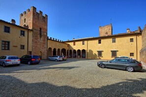 A courtyard with a historic building featuring a tower and arches, surrounded by parked cars.