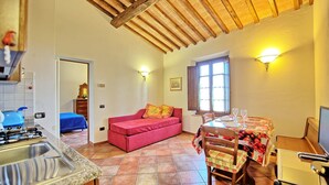 A cozy room with a kitchen, a dining area with a table set for two, and a red sofa with sunflowers. - Nice apartment for 3 guests with WIFI, A/C, TV and panoramic view, close to San Gimignano (Certaldo)