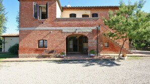 Un bâtiment à deux étages, construit en briques, avec une entrée centrale, un petit balcon à l’étage supérieur et une allée gravillonnée.