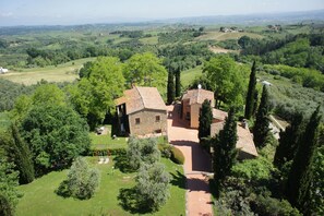 A stone farmhouse with a red-tiled roof, surrounded by lush greenery and rolling hills.