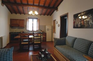 A living room with a sofa, a dining table with chairs, a kitchen with a refrigerator, and a window with curtains.