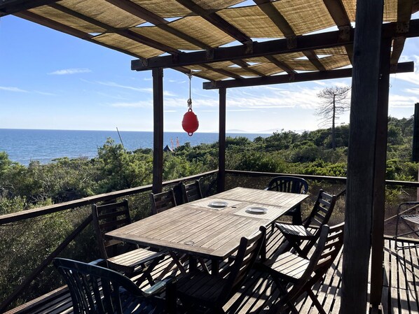 A wooden deck with a table and chairs, overlooking a body of water and greenery.