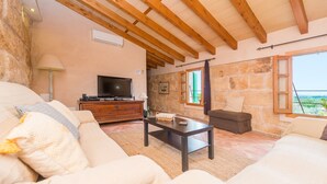 Una sala de estar acogedora con pared de piedra, vigas de madera, televisor y asientos cómodos.