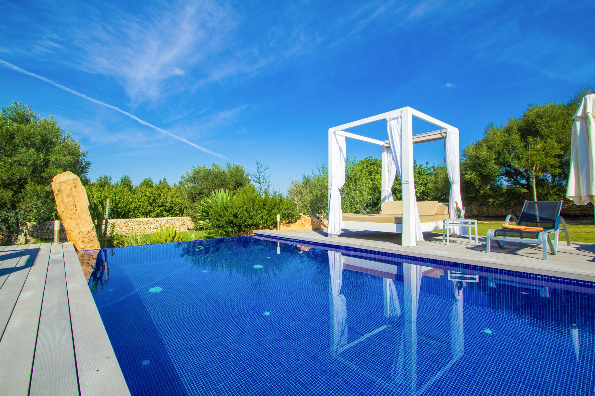A clear blue swimming pool with a wooden deck, a white gazebo, and outdoor seating.