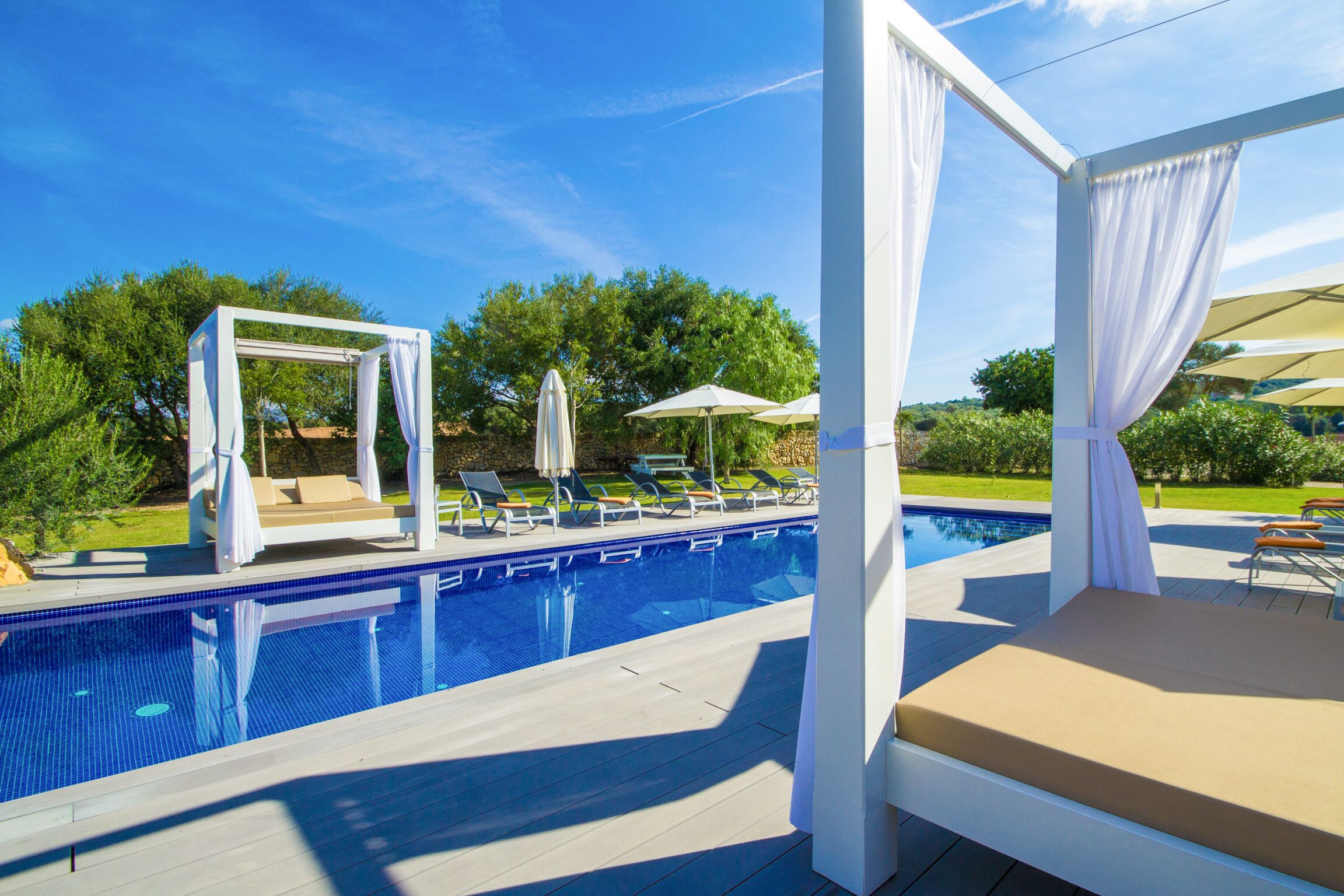 Un área de piscina con una piscina azul cristalina, cabañas blancas y sillones de descanso.