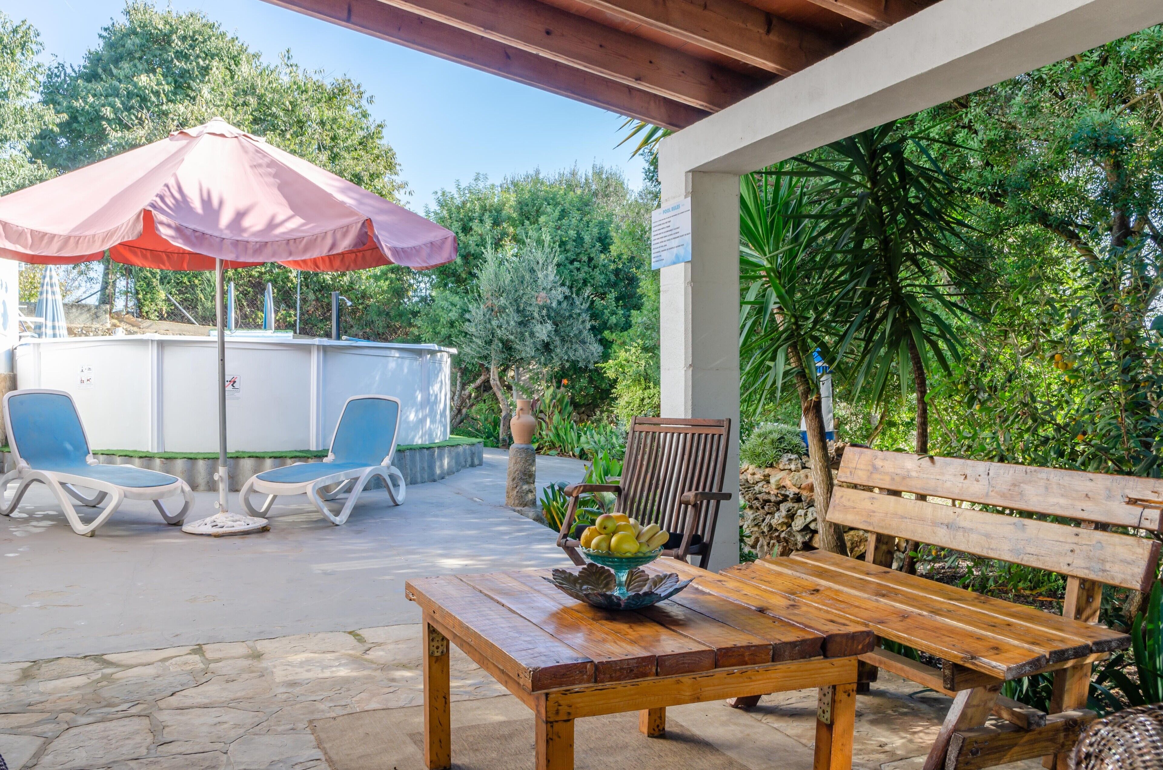 Une terrasse extérieure avec une table en bois, deux fauteuils de jardin bleus, un banc en bois et un parasol rose.