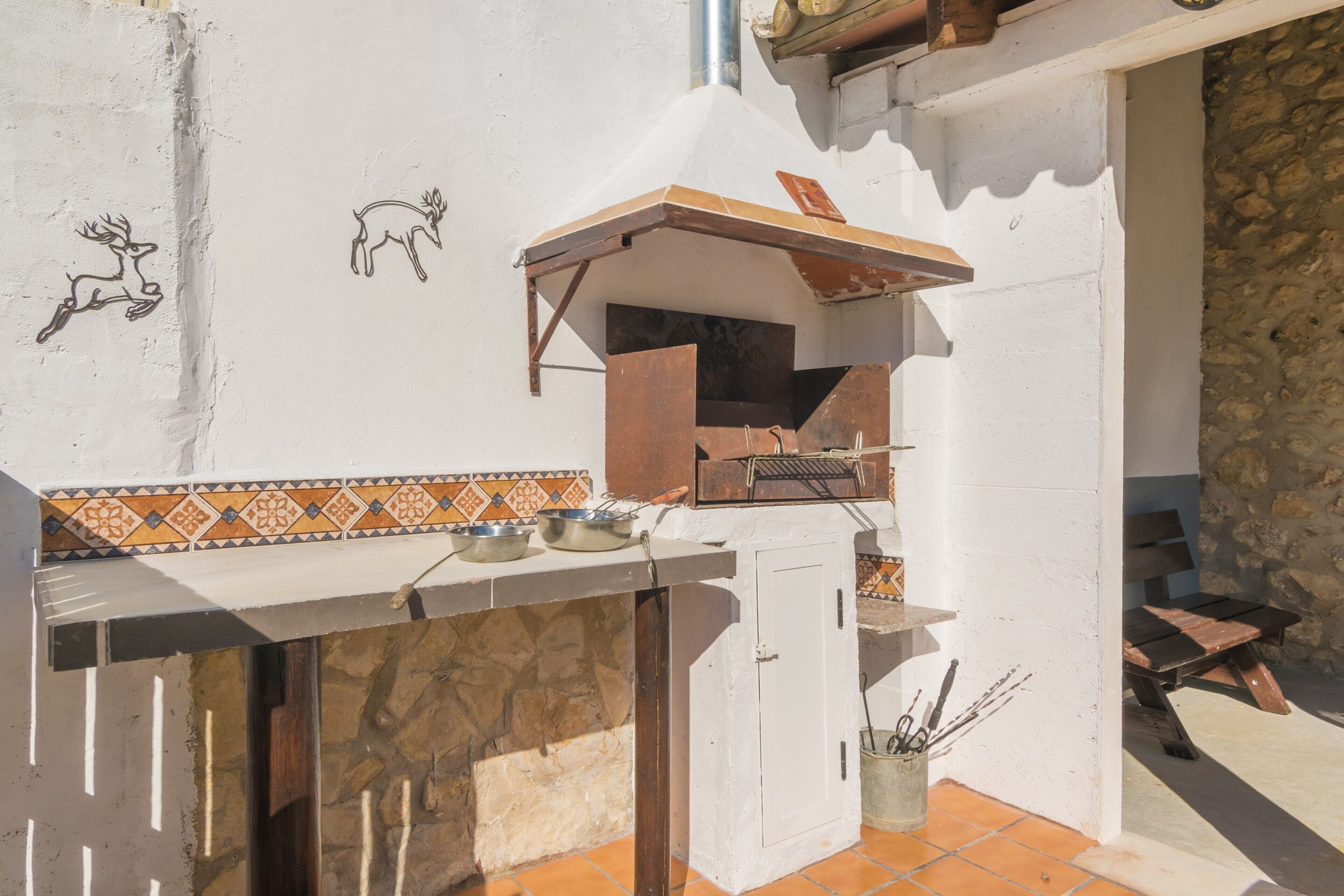 An outdoor kitchen area with a grill, cooking utensils, and decorative wall art.