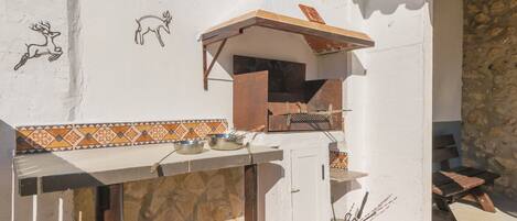 An outdoor kitchen area with a grill, cooking utensils, and decorative wall art.