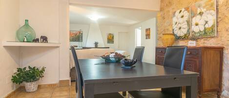 A dining area with a dark wooden table, black chairs, and a bowl of fruit. There is a potted plant on the floor and a vase on the wall.